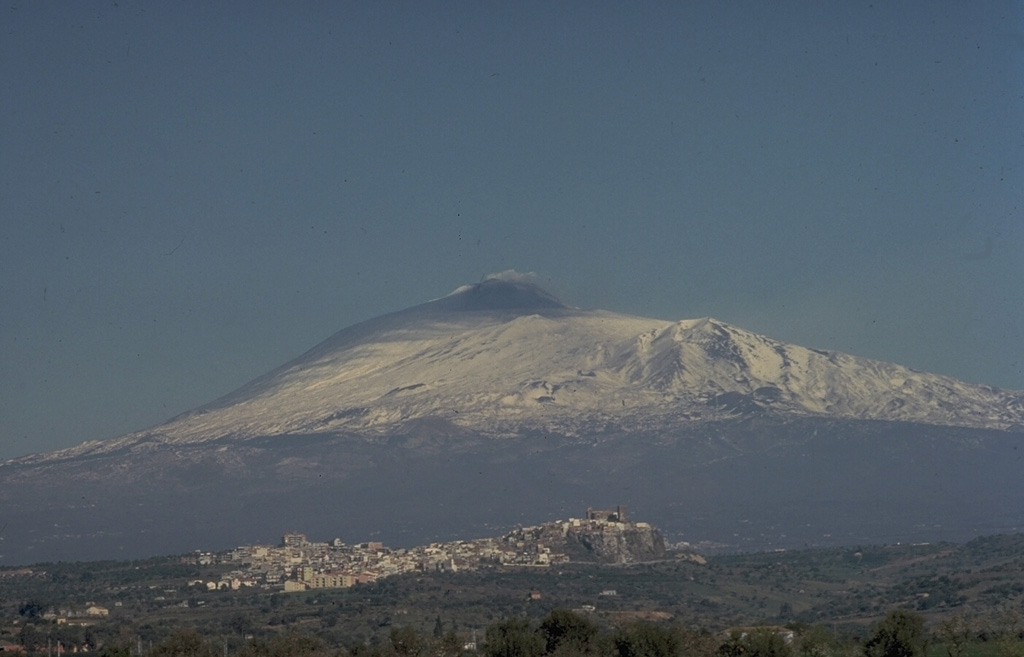 Snow-capped Mount Etna, seen here from the SE, rises more than 3 km above the coastline of Sicily.  The massive basaltic stratovolcano is 60 km by 40 km in width.  Its summit is truncated by several small calderas, and the Valle de Bove, a 5 x 10 km horseshoe-shaped depression created by incremental landsliding, extends to the eastern coast.  Persistent summit eruptive activity is punctuated by intermittent eruptions from cones and fissures that dot its massive flanks. Copyrighted photo by Katia and Maurice Krafft.