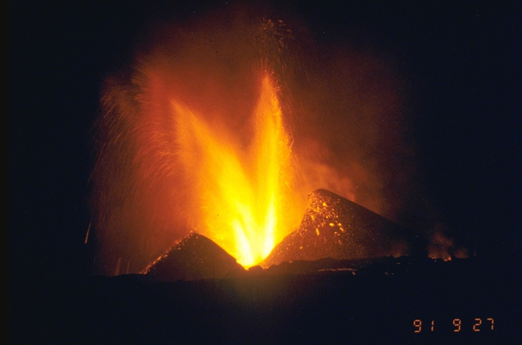 An eruption began on 20 September 1991 on the NE flank, 15 km from the summit. This was the northernmost historical eruption site of Nyamuragira. Lava fountaining from the new Mikombe cone is seen here on 26 September (the 27 September date-time stamp is in Japan Standard Time). Lava flows extended 6-7 km to the NE, cutting the road to Tongo. The eruption became more explosive on 20 November, and by July 1992 had built 26 scoria cones along a NE-trending fissure zone. The eruption continued until 8 February 1993. Photo by Minoru Kasahara, 1991 (Hokkaido University).