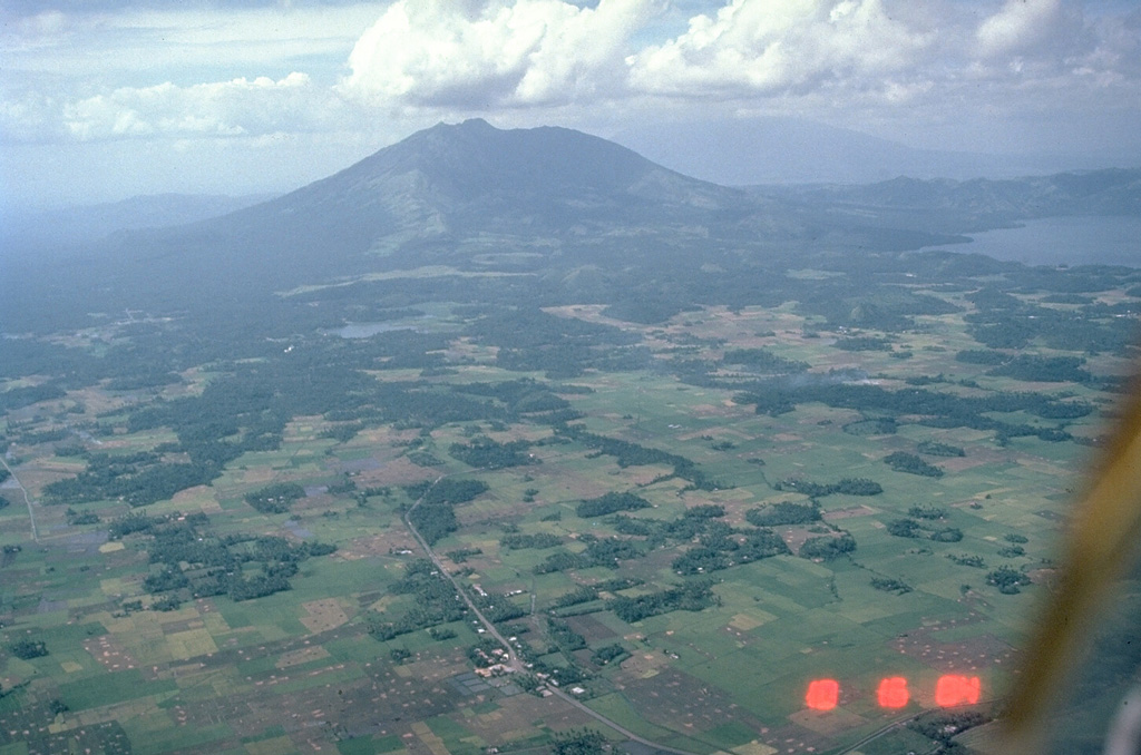 The entire foreground area in this view of Iriga volcano is a massive 1.5 km3 debris avalanche deposit formed by a Holocene landslide. This view from the SE shows the typical hummocky debris avalanche topography. Many of the darker areas are tree-covered hummocks; the irregular topography of the also creates many small ponds. Photo by Chris Newhall (U.S. Geological Survey).