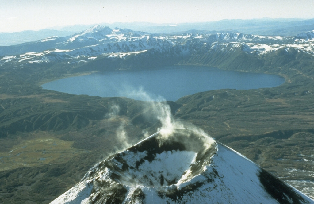 The lake-filled Akademia Nauk caldera, seen here from the north with Kaymsky in the foreground, is one of three volcanoes constructed within a large mid-Pleistocene caldera. Two nested calderas, 4 x 5 km Odnoboky and 3 x 5 km Akademia Nauk formed during the late-Pleistocene. The first historical eruption from Akademia Nauk took take place on 2 January 1996, when a brief, day-long explosive eruption occurred from vents beneath the NNW part of the caldera lake. Photo by Dan Miller (U.S. Geological Survey).