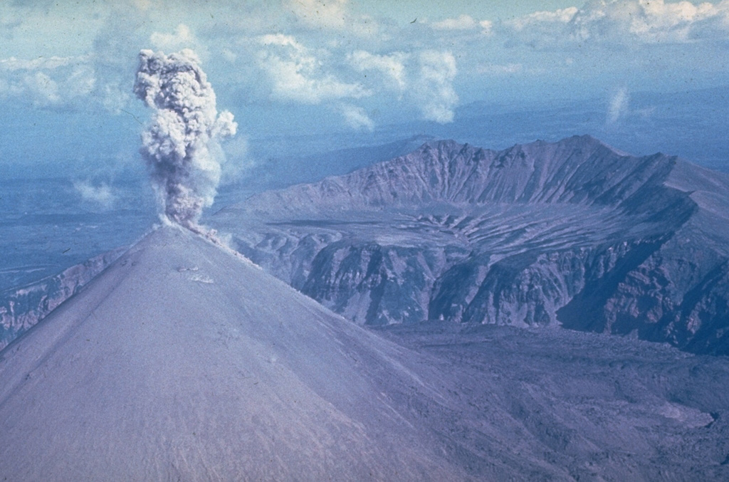 This ash plume rising above the summit of Karymsky during the early 1970's represents typical activity during its 1970-1982 eruption. It was constructed within a 5-km-wide caldera that formed about 6,000 years ago. The northern Karymsky caldera wall is seen across the center of the photo. It formed within the older Dvor caldera, with the caldera wall visible in the background. Photo by Yuri Doubik, 1972 (Institute of Volcanology, Petropavlovsk).
