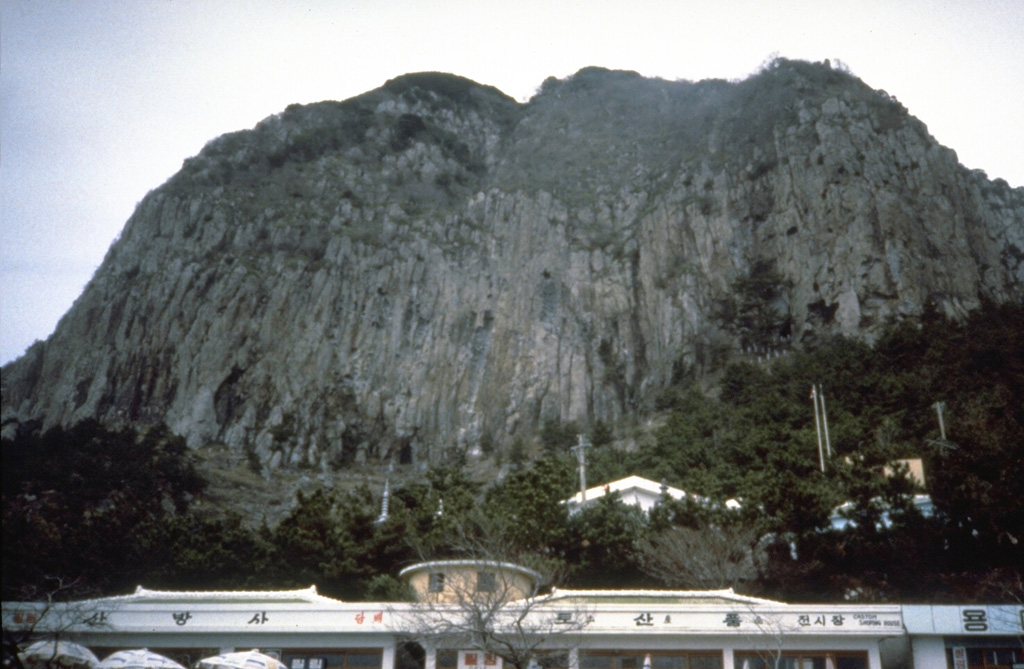 Prominent columnar jointing is visible on the steep sides of a trachytic lava dome on the southern coast of Cheju Island. A cluster of trachytic lava domes were erupted near the end of the second stage of activity of Halla, during which the shield volcano was formed in the center of the island. Photo by Norm Banks, 1980 (U.S. Geological Survey).