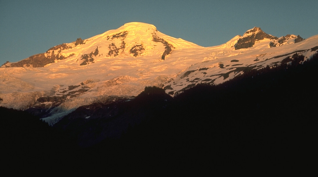 Mount Baker is seen here from the Glacier Creek valley on the NW side. Coleman Glacier is in the right-center of the photo with Coleman Saddle located between the summit and Colfax Peak on the right. The active Sherman Crater is on the opposite SE side of the summit. Photo by Lee Siebert, 1972 (Smithsonian Institution).