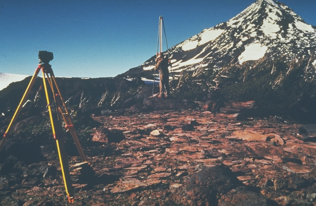 U.S. Geological Survey scientists monitor deformation on the Three Sisters volcanoes in the central Oregon Cascades, with Middle Sister volcano in the background. Precise leveling that permits detection of minor uplift is one of several monitoring techniques used to forecast eruptions. Photo by John Ewert, 1985 (U.S. Geological Survey).