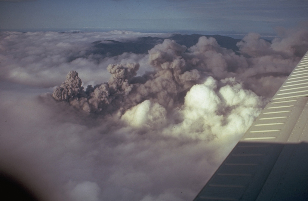 A dark ash plume at Arenal rises above white atmospheric clouds in 1968. A major explosive eruption began on 29 July 1968 from three new craters down the western flank. A series of major explosions took place between the morning of 29 July and the afternoon of 31 July. Photo by Tom Simkin, 1968 (Smithsonian Institution).