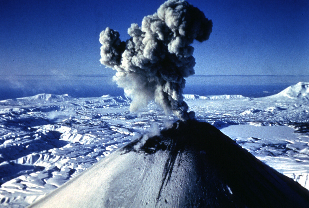 An ash plume rises above the summit of Karymsky in January 1996. Explosive eruptions began on 2 January from the summit and SW flank. On the same day a powerful explosive eruption took place from Akademia Nauk caldera, the smooth area to the right. The Akademia Nauk eruption lasted only a day, but long-term activity continued at Karymsky. Photo by Nikolai Smelov, 1996 (courtesy of Vera Ponomareva, Institute of Volcanic Geology and Geochemistry, Petropavlovsk).