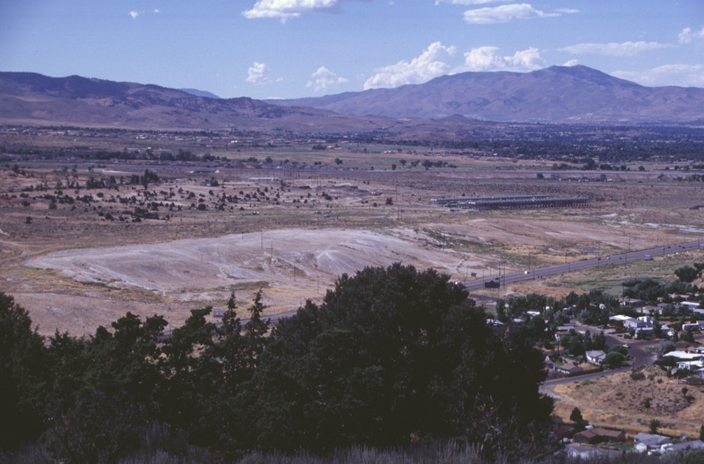 The light-colored area at the left-center is the Main Terrace, which formed along the principal fissure of the Steamboat Springs geothermal field.  The N-S-trending fissure deposited siliceous sinter from hot waters that issued from surface faults and traveled down slope towards U.S. Highway 395, which cuts diagonally across the bottom of the photo.  The linear structure at the right-center is the power generating plant of the geothermal field.  Out of view below the trees at the lower left is the Steamboat Resort, which dates back to the 1860s. Photo by Lee Siebert, 1998 (Smithsonian Institution).