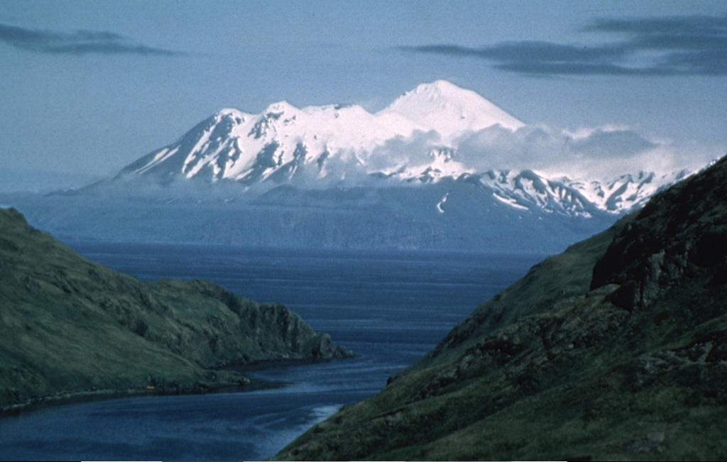Great Sitkin in the Andreanof Islands is seen here from Finger Bay on Adak Island. The edifice was constructed within a caldera, part of which forms the high snow-covered peak to the right. The post-caldera cone contains a 0.8 x 1.2 km ice-filled summit crater. The rim forms the irregular summit on the left horizon. A lava dome 400-600 m wide was emplaced through a glacier in 1945. Photo by Fred Zeillemaker, 1982 (U.S. Fish and Wildlife Service, courtesy of Alaska Volcano Observatory).