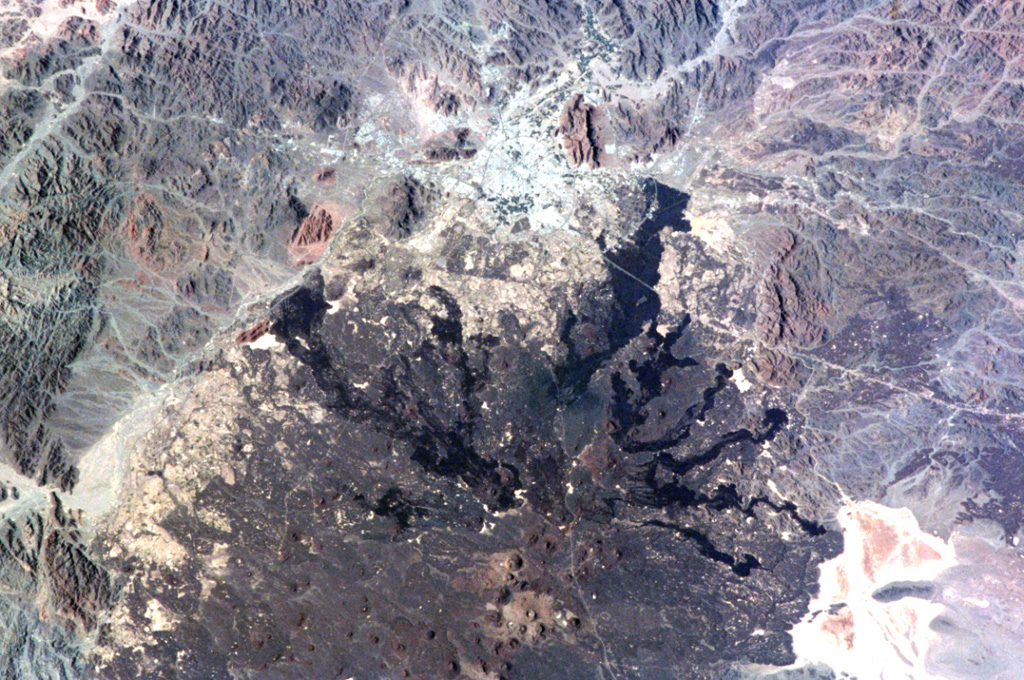 The northern part of Saudi Arabia's largest lava field, 20,000 km2 Harrat Rahat, is seen in this NASA International Space Station image (N to the top left). Harrat Rahat extends for 300 km S of the city of Madinah (Medina), the light-colored area at the top-center. Although basaltic scoria cones are more common, small shield volcanoes and lava domes are also present. The most well-known eruption took place in 1256 CE, when the large dark-colored flow seen extending to the upper right traveled 23 km to within 4 km of Madinah. NASA International Space Station image ISS001-344-27, 2001 (http://eol.jsc.nasa.gov/).