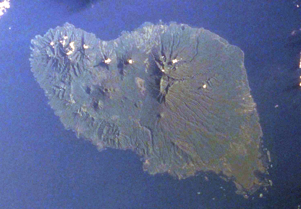 The 50-km-long island of Umboi, the largest of the volcanic islands off the north coast of New Guinea, is seen in this Space Shuttle image (N is to the top-right). A large 13 x 17 km caldera is visible in the northern half of the island and is breached to the NE (top center). Three post-caldera cones with summit crater lakes (left center) are visible on the smooth-surfaced caldera floor. The large eroded massif (right center) is an older volcanic complex, as is the dissected northern tip of the island (upper left). NASA Space Shuttle image STS50-99-748-47, 2000 (http://eol.jsc.nasa.gov/).