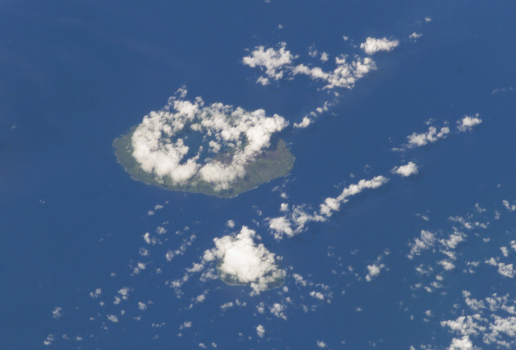 Clouds almost entirely obscure the small island of Kao (lower-center) in this NASA International Space Station image, and a circular cloud pattern rises above the caldera rim of the larger island of Tofua (left-center). No historical eruptions are known from Kao, and fresh-appearing lava flows are not seen, although the absence of sufficient time for erosion to produce deep gullies or high sea cliffs suggests a very recent origin. NASA International Space Station image ISS008-E-14026, 2004 (http://eol.jsc.nasa.gov/).