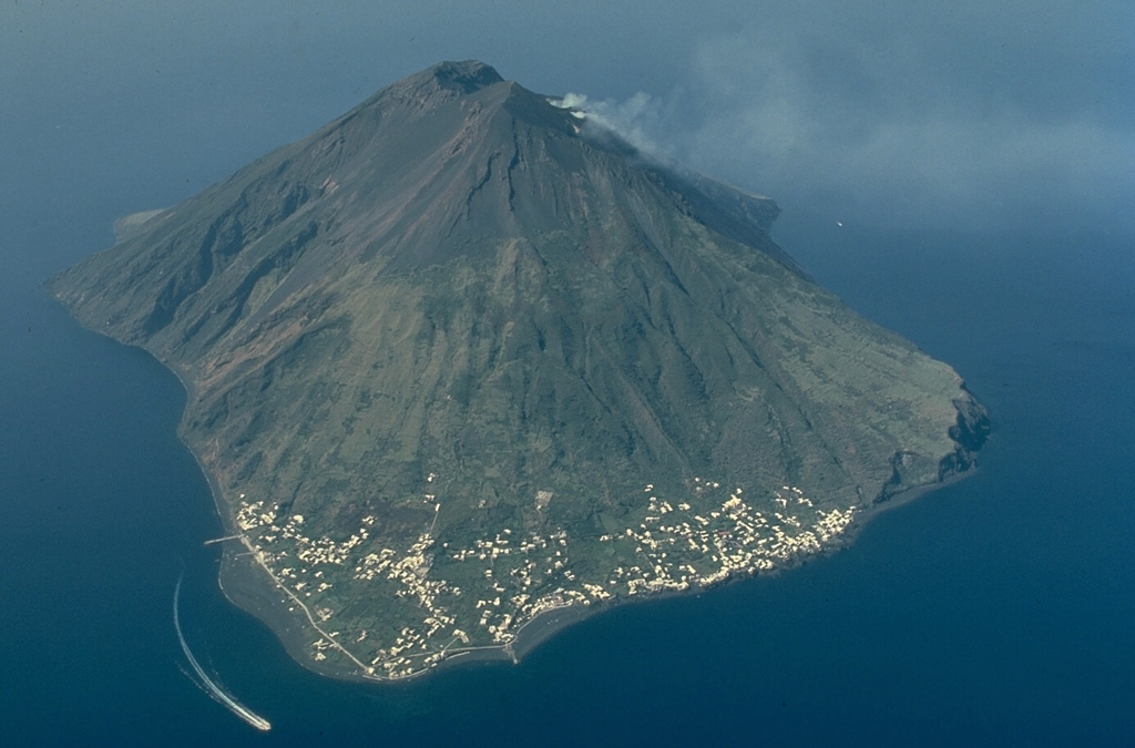 Villages cling to the only relatively flat area on the island of Stromboli, seen here from the NE.  Stromboli, known as the "Lighthouse of the Mediterranean," has been in continuous eruptive activity for at least 1300 years.  It is the type locality for "strombolian" eruptions, moderate explosive eruptions that eject ash and incandescent bombs.  Steam rises from the active vent at the head of the Sciara del Fuoco near the summit of the 924-m-high volcano.  Copyrighted photo by Katia and Maurice Krafft.