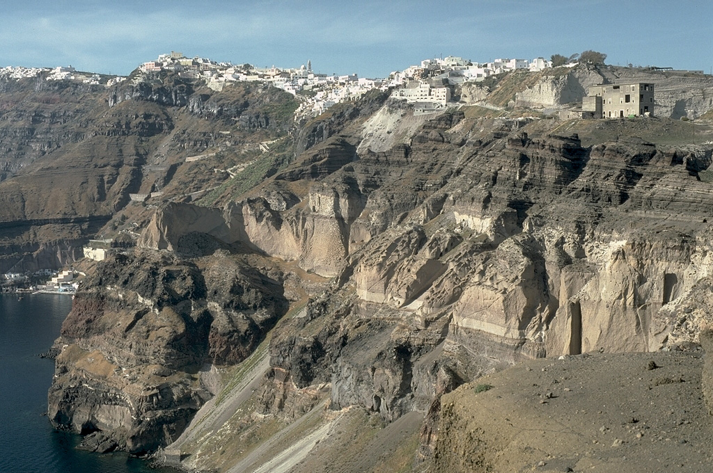 The steep eastern caldera walls of Santorini are draped by the town of Firá, many of which were built within deposits of the Minoan eruption that took place about 3,500 years ago. The most prominent unit in the caldera wall at this location is the Middle Tuff Sequence, the lighter-colored, cliff-forming unit halfway up the wall that is composed of a basal pumice deposit overlain by breccia and pyroclastic flow deposits. The Middle Tuff and the darker bedded layers overlying it were deposited during late-Pleistocene eruptions. Photo by Lee Siebert, 1994 (Smithsonian Institution).