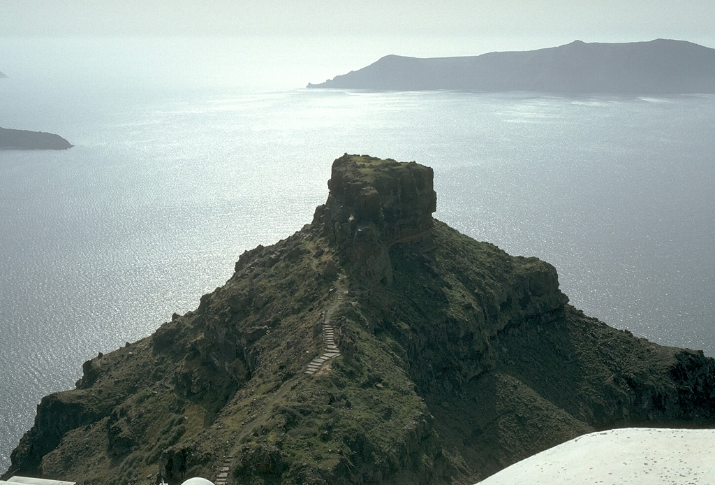 The steep inner walls of Santorini drop steeply into the caldera bay. Pyroclastic flow deposits from four caldera-forming eruptions dating back to 100,000 years ago are exposed in the caldera walls in this N-looking view. The youngest caldera was formed about 3,500 years ago during the Minoan eruption of Santorini. The flat-topped peak on the left skyline is Skaros, a remnant of a shield volcano constructed within a previous caldera. Photo by Lee Siebert, 1994 (Smithsonian Institution).