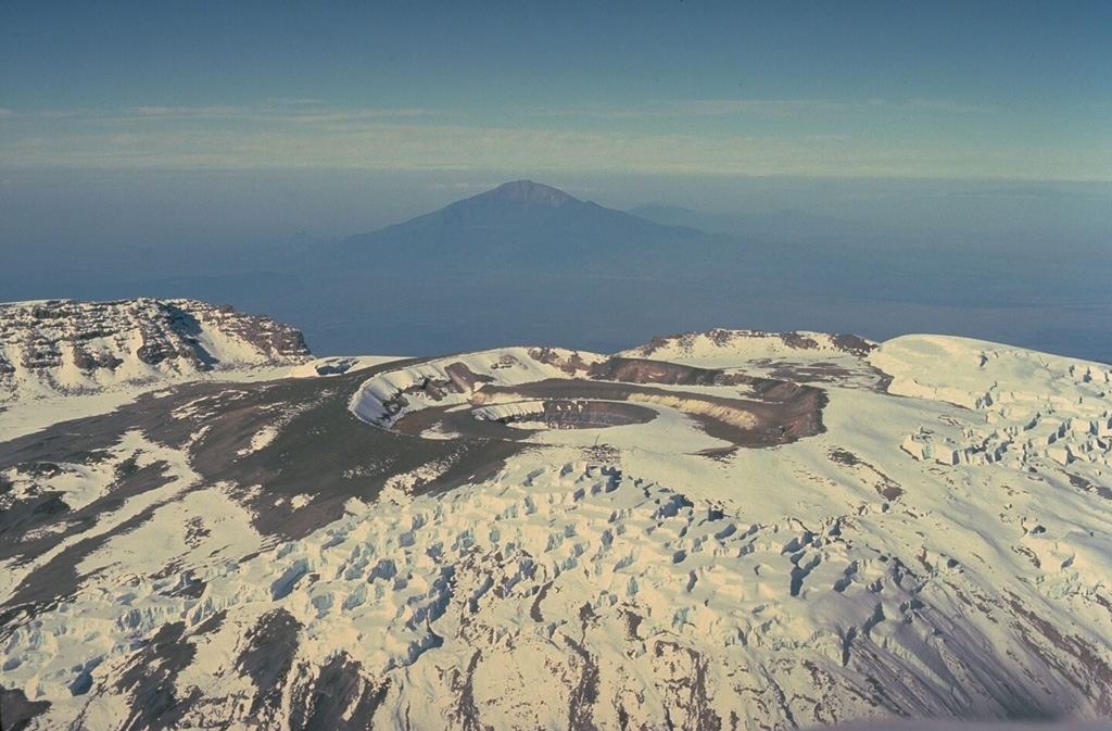 An aerial view across the summit plateau of Kilimanjaro looks west towards Meru stratovolcano in the distance.  The nested craters in the center are the youngest features of the volcano.  They cut a summit ash cone that has grown within a 2.4 x 3.6 caldera, whose rim is seen at the left. Copyrighted photo by Katia and Maurice Krafft, 1977.