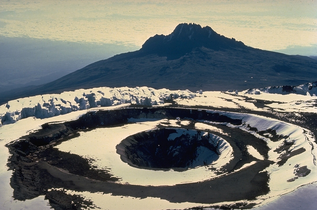 A cluster of nested craters occupies the summit of Kilimanjaro volcano.  This view looks ESE to Mawenzi, a dissected stratovolcano that is one of three forming the broad Kilimanjaro massif.  The low ridge above the crater complex at the left is part of the steep-sided summit icecap.  The coalescing volcanoes of Mawenzi, the central summit cone of Kibo, and Shira to the NW form the elongated Kilimanjaro massif,  Africa's highest peak. Copyrighted photo by Katia and Maurice Krafft, 1977.