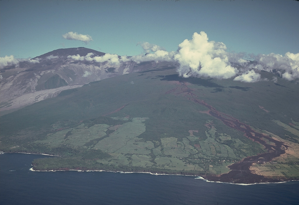 The massive Piton de la Fournaise on the island of Réunion is one of the world's most active volcanoes. It is seen here in 1977 with a black lava flow descending the outer NE flank to the sea. The unvegetated summit (top left) was constructed within an 8-km-wide caldera that is breached to the sea. Its sloping N rim is marked by the diagonal vegetation line at the left. More than 150 eruptions have occurred since the 17th century, mostly from vents within the caldera. Copyrighted photo by Katia and Maurice Krafft, 1977 (published in SEAN Bulletin, 1977).