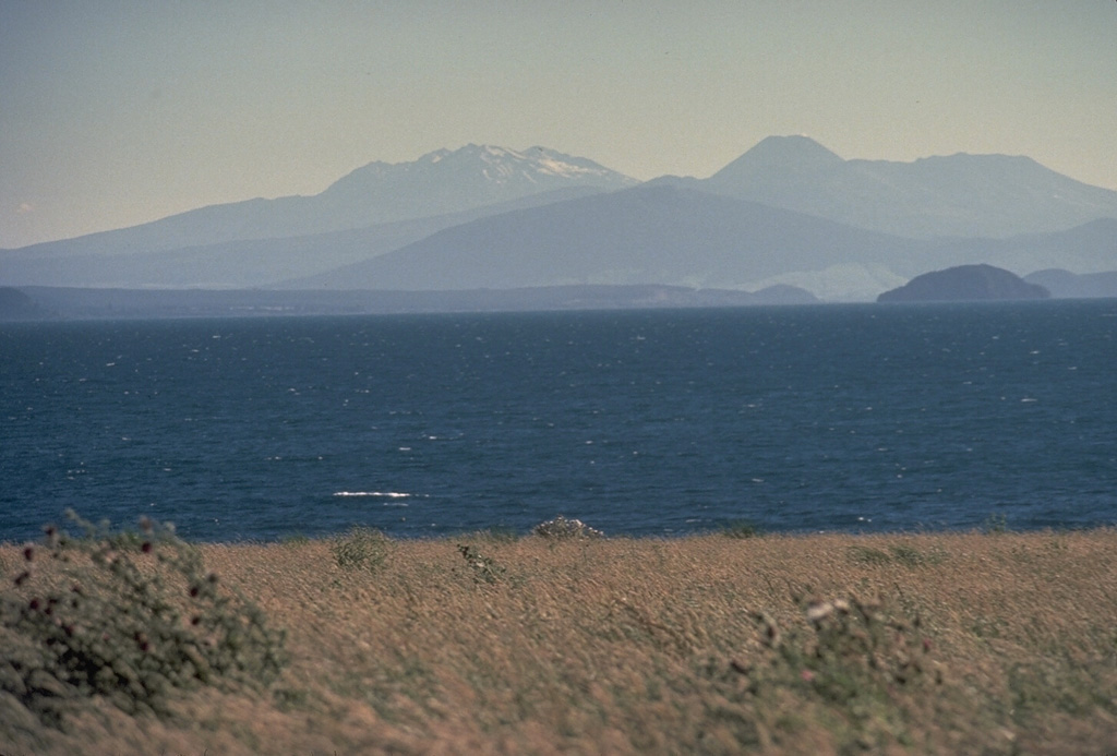 This view looking SW across Lake Taupo, the southernmost major caldera of the Taupo Volcanic Zone, shows several major peaks of Tongariro and Ruapehu. The broad forested peak below the center horizon is the Pleistocene Pihanga volcano. The steep-sided cone on the horizon to its right is Ngauruhoe, the youngest cone of the Tongariro complex. The broad massif to its right is Tongariro. The snow-capped massif on the left-center horizon is Ruapehu. Photo by Tom Simkin, 1986 (Smithsonian Institution).
