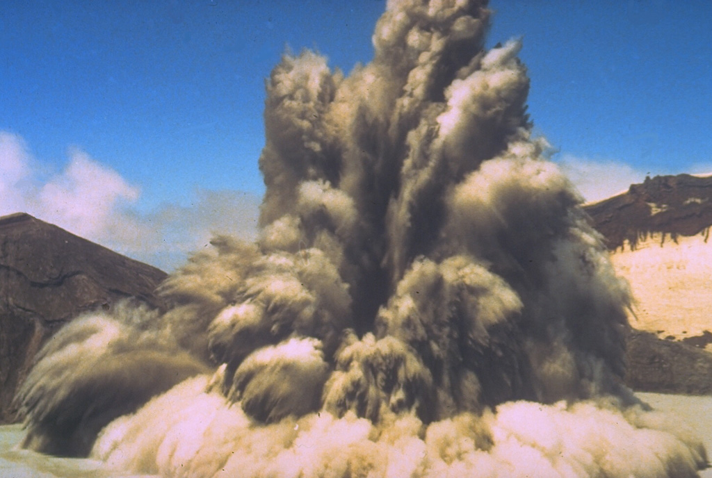 The interaction of magma and water can produce strong phreatic (steam-driven) explosions, such as in this 1980 photo of New Zealand's Ruapehu volcano. Ash and steam trail from large ejected blocks in the eruption column. Pyroclastic surge can be seen traveling radially along the surface of a crater lake. Phreatic or phreatomagmatic explosions are common at submarine volcanoes, crater lakes, and other places where hot magma (or associated gases) encounters surface water or groundwater. Photo by Hollick, 1980, courtesy of Bruce Houghton (Wairakei Research Center).