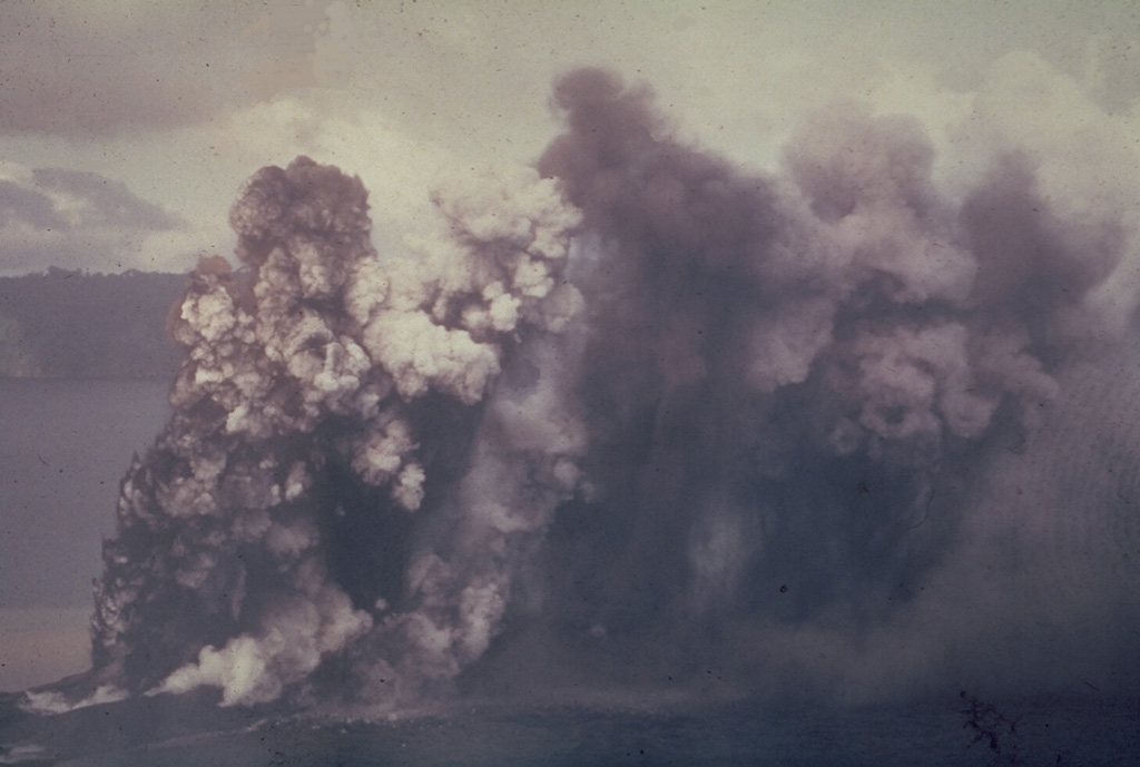 An ash plume rises above Motmot Island within the Lake Wisdom caldera of Long Island in 1953. Explosions that ejected ash and lapilli began on 8 May. Intermittent explosive activity continued until 7 January 1954.  Photo by John Best, 1953 (courtesy of Wally Johnson, Australia Bureau of Mineral Resources).