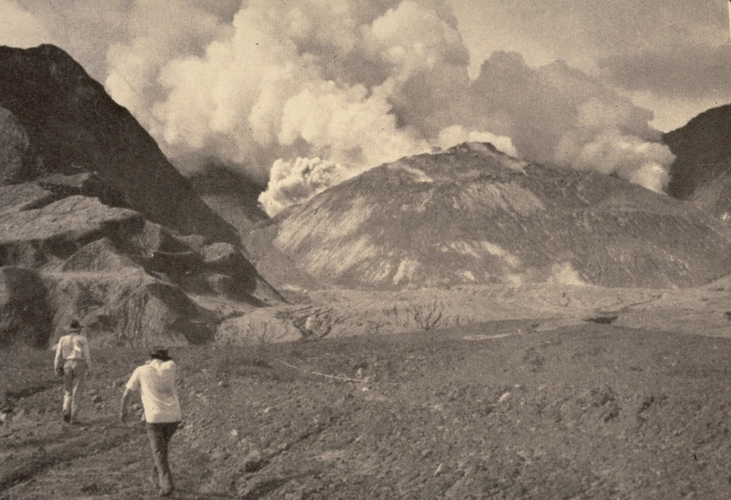 Members of a scientific team approach the crater of Mount Lamington through the avalanche valley on 11 February 1951. Explosions occurred from a vent behind the new lava dome growing in the summit crater produce gas and ash plumes. Growth of the lava dome began soon after the catastrophic 21 January explosive eruption. At the time of this photo, the smooth-surfaced lava dome was uplifting the floor of the new crater. The dome eventually grew to the height of the crater rim. Photo by Tony Taylor, 1951 (Australia Bureau of Mineral Resources).