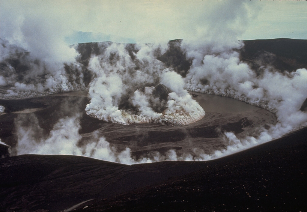 The degassing crater of Galunggung volcano on 5 February 1983, a month after the end of the 1982-83 eruption. Plumes are shown rising from a late-stage scoria cone that formed in the center of the crater and from the margins of the crater wall. A lake that had begun to form in the crater at the time of this photo eventually grew to cover the cone. Photo by Don Peterson, 1983 (U.S. Geological Survey).
