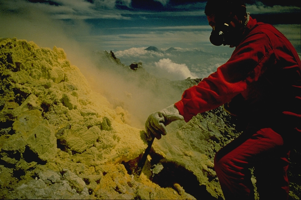 Volcanologist Maurice Krafft measures the temperature of a sulfur-encrusted fumarole during a 1971 trip to the summit of Merapi volcano in central Java.  Gas masks are essential when working around the toxic fumaroles.  The temperatures of selected fumaroles on the summit of Merapi are measured regularly by the Volcanological Survey of Indonesia as a part of their program to monitor the hazardous volcano.  Sumbing (left) and Sundoro (right) volcanoes appear on the distant horizon to the NW. Copyrighted photo by Katia and Maurice Krafft, 1971.