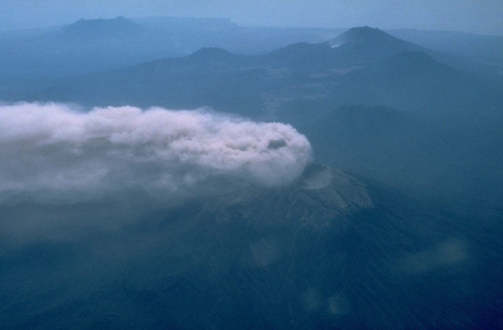 An aerial view from the SW on 12 September 1991 shows an eruption plume from Raung volcano in eastern Java dispersed to the NW by strong winds. Behind Raung is Ijen caldera, capped by the post-caldera cone of Gunung Merapi (upper right). The light spot below and to the left of Merapi is Kawah Ijen, a renowned crater lake. The flat-topped volcano at the upper left is Gunung Baluran, which occupies the NE-most tip of the island of Java. Photo by Jeff Post, 1991 (Smithsonian Institution).