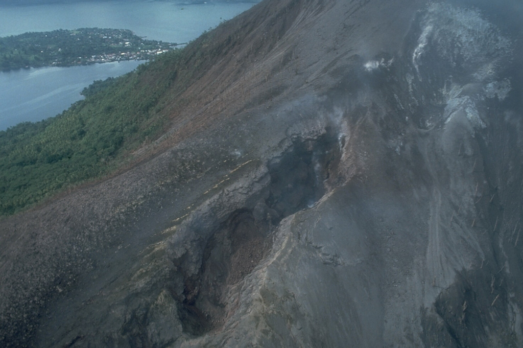 Fissures of vents no. 1 (bottom) and 3 (upper right) cut the northern flank of Banda Api volcano.  Ash mantles vegetation adjacent to the fissures, which are about 15-20 m wide at this location.  These vents, which began erupting on May 9, 1988, also fed two large lava flows that reached the sea along the northern and NW coasts.  Neira Island appears in the background in this May 21, 1988 photo. Photo by Tom Casadevall, 1988 (U.S. Geological Survey).