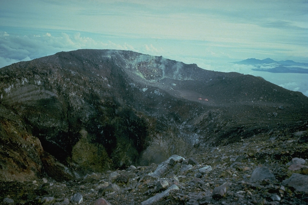 The summit crater of Gamalama volcano on Ternate Island, seen here from the south rim, contains a steep-walled inner crater that is 150 x 180 m wide and 100 m deep.  The western coast of Halmahera Island appears in the distance at the right. Copyrighted photo by Katia and Maurice Krafft, 1976.