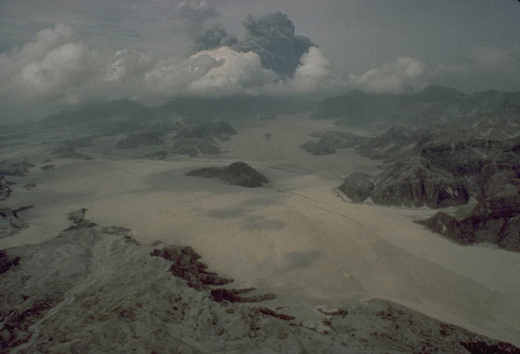 Voluminous pyroclastic flows on 15 June 1991 descended all sides of Mount Pinatubo in the Philippines. The flat, light-colored areas in the foreground are pyroclastic flow deposits that filled the Marella River valley on Pinatubo's SW flank to a depth of 200 m. The dark hill at the center was completely surrounded by pyroclastic flows that traveled 14 km down this valley. Photo by Rick Hoblitt, 1991 (U.S. Geological Survey).