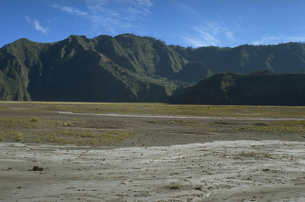Two caldera walls can be seen in this view across the flat Sandsea caldera floor. The low ridge in the shadow in the foreground is the northern wall of the younger Tengger (Sandsea) caldera, which merges at the upper left with the background ridge, the northern wall of the 16-km-wide Ngadisari caldera. Photo by Lee Siebert, 1995 (Smithsonian Institution).