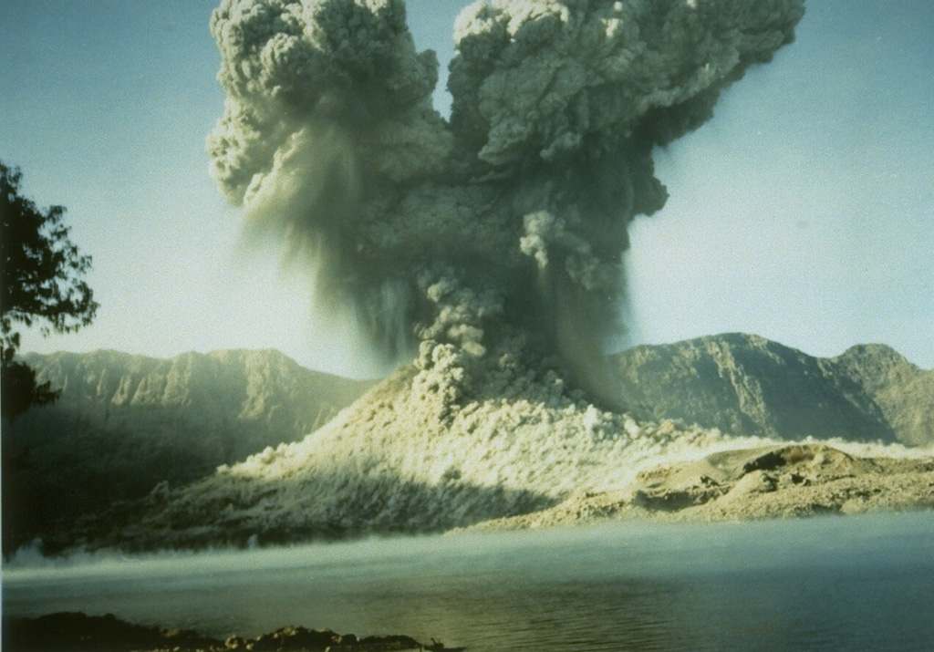 A 2-km-high ash plume rises above Barujari cone at Rinjani volcano on 9 June 1994 in this view looking S across the caldera lake with the Segara Anak caldera wall in the background. A small pyroclastic flow can be seen descending from the crater. The 1994 eruption began on 3 June and lasted until 21 November. Photo courtesy of Volcanological Survey of Indonesia, 1994.