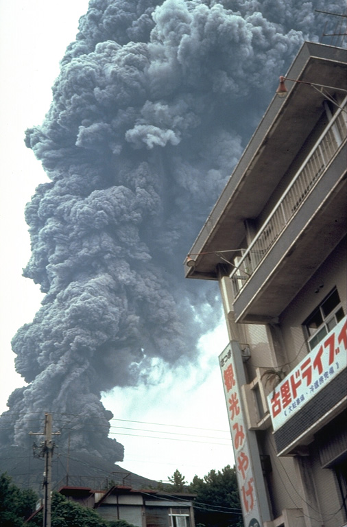 An ash plume rises above a restaurant on Sakurajima island in September 1981. Near-continuous periods of explosive eruptions have been occurring since 1955, frequently depositing ash on residential areas. Occasional larger explosions have ejected ballastic blocks that have penetrated concrete roofs of buildings. Villages are located along the island's coast, but most are only 3-5 km from the active Minamidake summit crater. Photo by Dick Stoiber, 1981 (Dartmouth College).