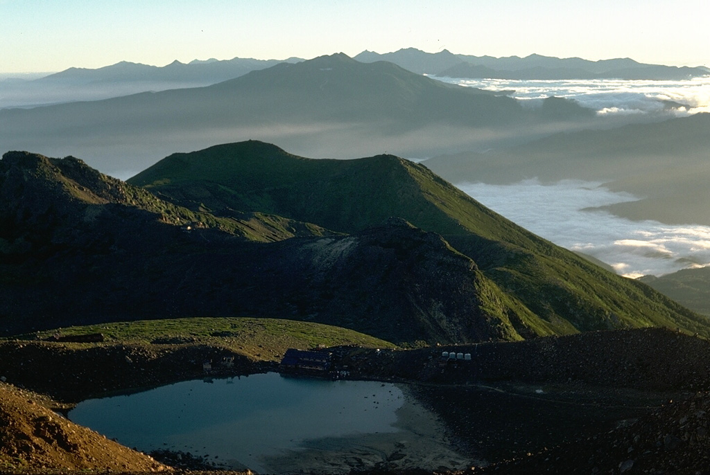 The summit of Ontake is shown here with the Northern Japan Alps on the horizon. Norikura, another Holocene volcano, forms the broad massif in the mid-distance. Ontake is constructed within a largely buried 4 x 5 km caldera. Ichinoike in the foreground is one of a series of small craters at the broad summit.  Photo by Lee Siebert, 1988 (Smithsonian Institution).