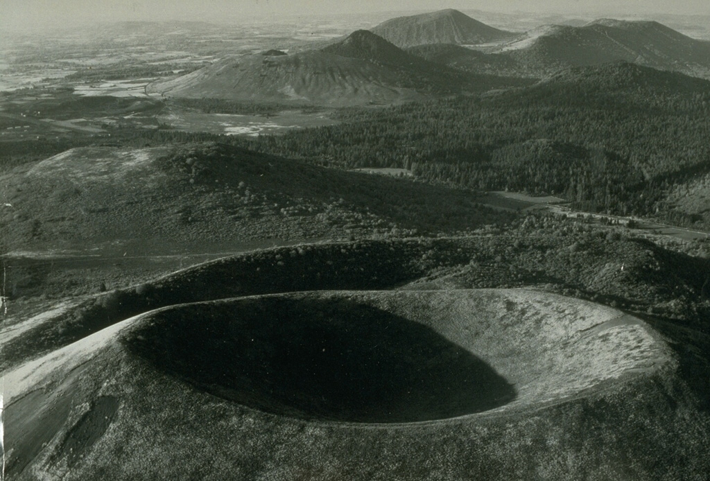 The Chaîne des Puys is a N-S-trending chain of cones, maars, and lava domes in the Auvergne region of France. The Puy de Pariou crater in the foreground is a tuff cone that grew about 8,200 years ago within an earlier tuff ring, whose rim appears immediately behind Pariou crater. A lava flow traveled 8 km W to near the present-day city of Clermont-Ferrand. The sharper peak in the background is Puy de Chopine, whose complex history ended with domal uplift. Photo by Loïc Jahan (Parc de Volcans, published in Green and Short, 1971).