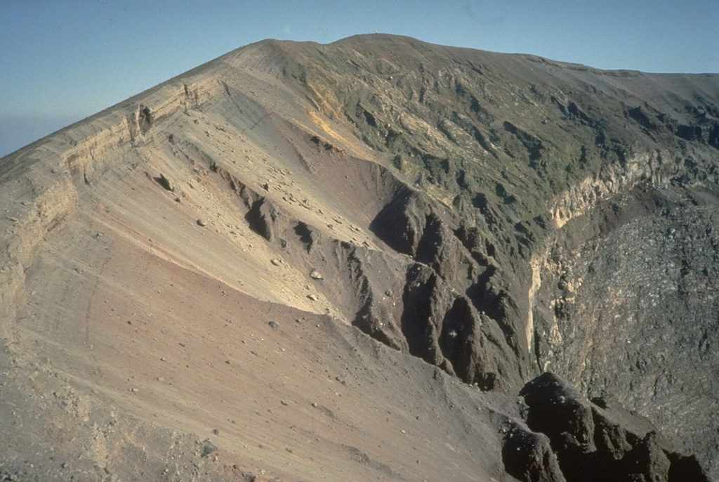The upper crater rim of Vesuvius is capped by thick tephra deposits from the last eruption episode in 1944. The bedded tephra layers overlie a light-colored layer at the right, a lava flow that had been erupted earlier in the 1944 eruption. The steep wall beneath the 1944 lava flow cuts through pre-1944 lava flows. Photo by Roberto Scandone, 1989 (University of Rome).