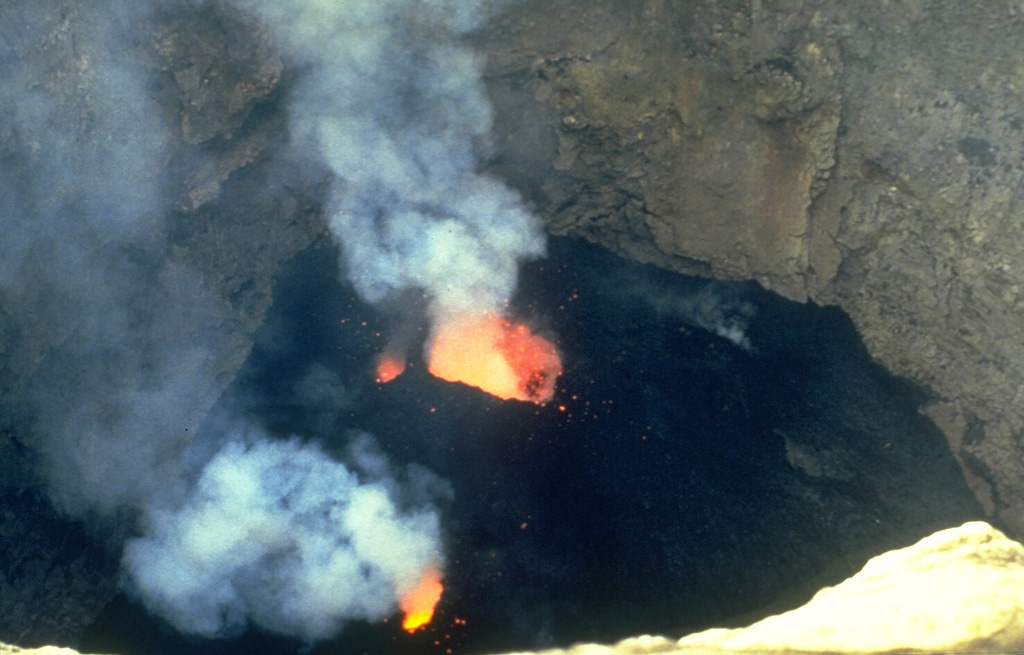 Weak Strombolian activity on 5 December 1985 from Bocca Nuova, one of two active vents in the Central Crater, is typical of persistent summit activity at Etna. Fresh black lava flows cover the floor of the crater. Both Bocca Nuova and the E vent, La Voragine, frequently eject scoria and molten lava bombs that commonly do not reach above the height of the roughly 100-m-high crater. Occasional periods of high lava fountaining and ash ejection also occur. Photo by Romolo Romano, 1985 (IIV-CNR, Catania, Italy).