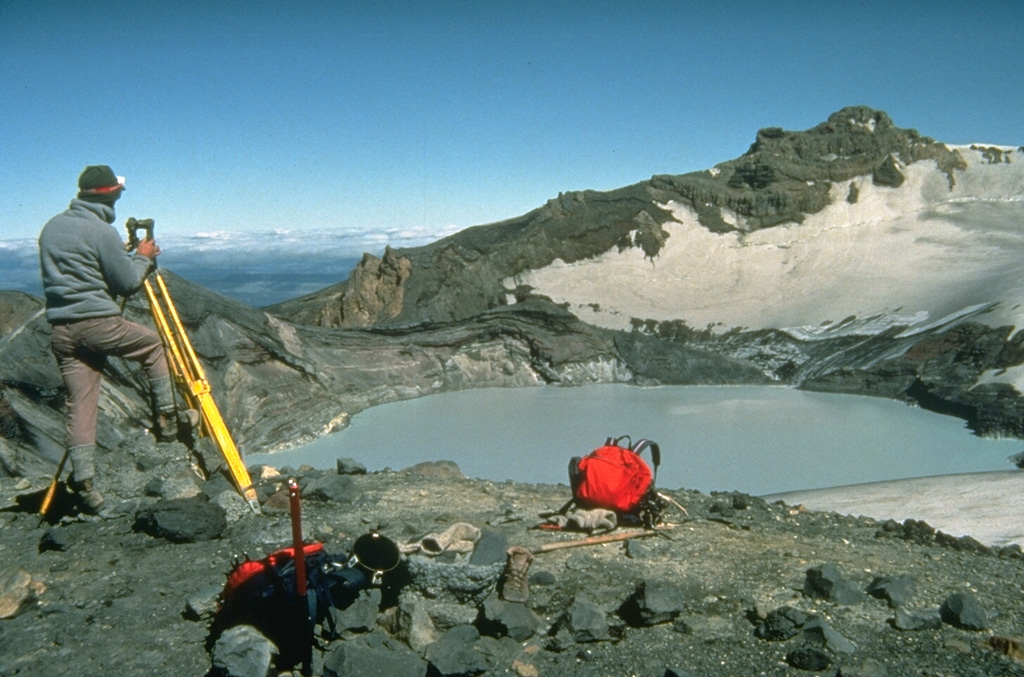 New Zealand volcanologist Brad Scott conducts theodolite (detecting height changes) measurements at Ruapehu’s Crater Lake in 1988. Measurements of the lake height, temperature, and chemistry are made routinely, and along with seismic instrumentation, are used to help forecast future activity of the volcano. Intermittent steam explosions from beneath the lake have produced lahars, which have damaged ski facilities on the upper flanks and structures in valleys below the volcano. Photo by Don Swanson, 1984 (U.S. Geological Survey).