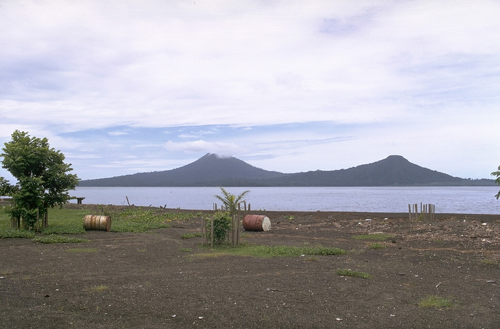 Lolobau volcano (left) is located on the western rim of a caldera that formed about 12,000 years ago on Lolobau Island. It is seen here from the south across Expectation Strait along the NE coast of New Britain. The peak at the right is on the eastern rim of the 6-km-wide caldera. Several vents within the caldera along an E-W-trending line on the E flank have had recorded activity. Photo by Robert Citron, 1970 (Smithsonian Institution; courtesy of William Melson)