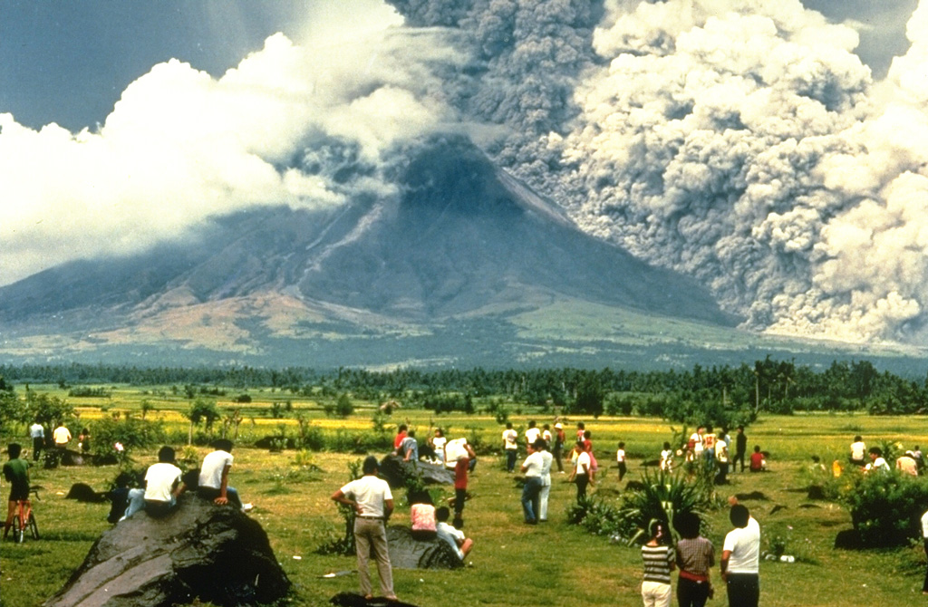 A crowd of spectators watches a pyroclastic flow sweeping down the SE flank of Mayon volcano on 24 September 1984. They stand on the surface of a deposit from a large lahar emplaced during an eruption in 1814. The pyroclastic flow seen here traveled about 6 km. Strong explosions the previous day created notches in the SE and east crater rims that funneled pyroclastic flows down ravines in those directions. Photo by Norm Banks, 1984 (U.S. Geological Survey).