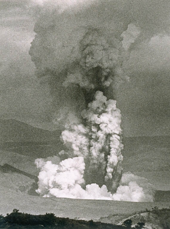 An ash plume rises above a vent on the SW side of Volcano Island at Taal on 30 September 1965, during a two-day eruption that began on the 28th. The white plume at the bottom is a horizontally moving base surge. The devastating pyroclastic surges caused 150 fatalities. Photo by L.E. Andrews, 1965 (courtesy of Jim Moore, U.S. Geological Survey).