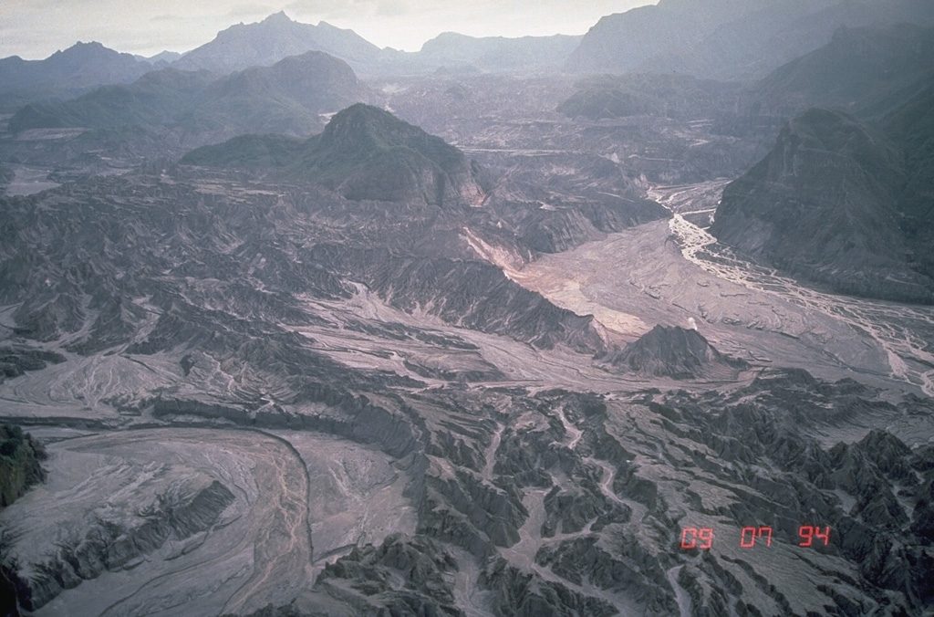 Thick pyroclastic flow deposits from the 1991 eruption of Pinatubo were rapidly eroded in the years following the eruption. This 7 September 1994 view of the upper Marella River valley from the SW, with the caldera rim on the skyline, shows the effects of the erosion of well over 100 m of pyroclastic flow deposits. Light-colored deposits in the channels at the middle right and lower left are post-1991 lahar deposits. Photo by Chris Newhall, 1994 (U.S. Geological Survey).