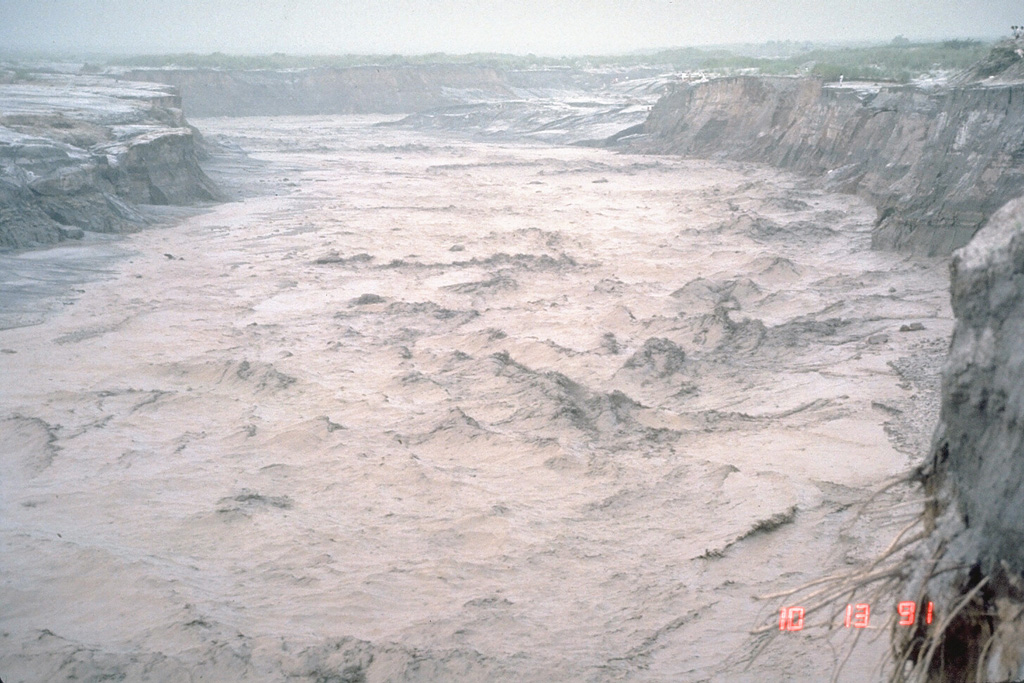 A lahar, or volcanic mudflow, fills the banks of the Pasig-Potrero River on the east side of Pinatubo volcano in the Philippines on 13 October 1991. The lahar moved at a velocity of 3-5 m/s and carried a few meter-sized boulders. This lahar was not directly produced by an eruption, but was triggered by minor rainfall that remobilized thick deposits of ash and pumice that blanketed the landscape. Devastating lahars occurred at Pinatubo for years after the catastrophic 1991 eruption. Photo by Chris Newhall, 1991 (U.S. Geological Survey).
