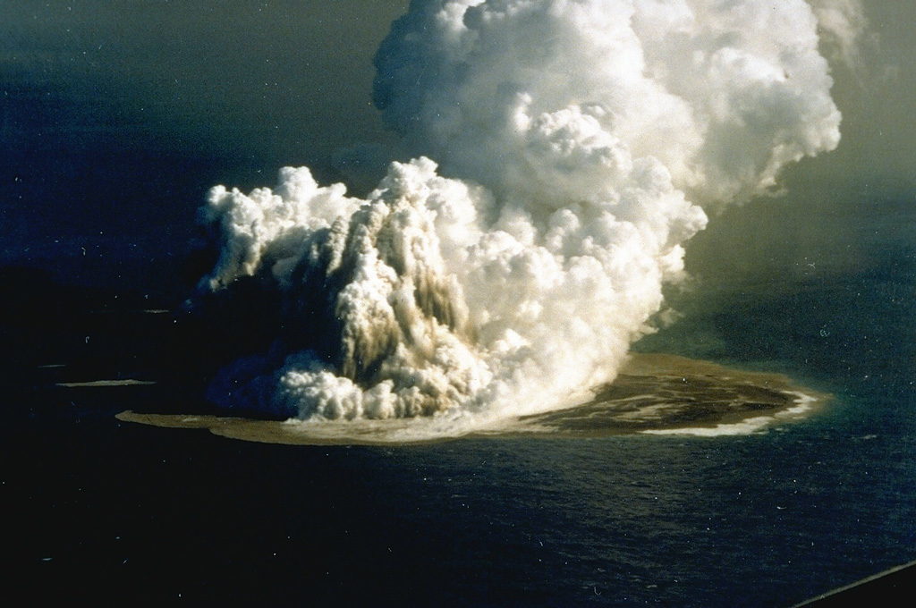 An eruption plume rising 3-4 km above Fukutoku-Oka-no-ba was witnessed from fishing boats on 18 Janaury 1986. A 4-km plume was detected by radar the following day. On 20 January a new island formed (seen here to the right of the eruption plume). The island reached maximum dimensions of 400 x 600 m, with a height of 15 m. Frequent strong explosions continued on 21 January, the day of this photo, and decreased in intensity that afternoon. Explosive activity ended by the next morning, and the island eroded to below sea level by 8 March. Photo by G. Iwashita, 1986 (Japan Meteorological Agency).