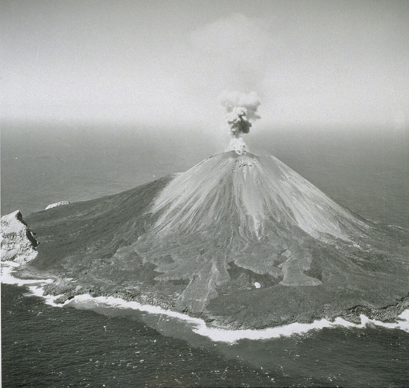 Explosive activity was frequently observed from Farallon de Pajoras volcano in October and November 1952. Lava flows were emplaced on the E and W sides of the summit in February-March 1953. This 1953 photo from the E shows a small plume rising above the summit crater and lighter-gray lava flows in the center that erupted in 1953. The lobe just left of center eventually reached the coast. Explosive activity continued until 15 April. The steep-sided peak on the SE coastline is a remnant of an older caldera. Photo by U.S. Navy, 1953.