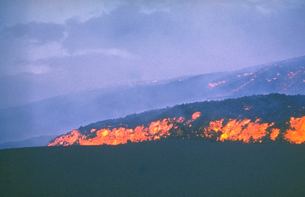 The incandescent lava flow front advances across an ash-covered surface in July 1975. Incandescence can also be seen in the main body of the flow behind it. This lava flow, the first of the "Great Tolbachik Fissure Eruption" of 1975-76, originated from the first of three large scoria cones that formed at the northern of two principal eruption sites. Photo by Anatolii Khrenov, 1975 (courtesy of Oleg Volynets, Institute of Volcanology, Petropavlovsk).