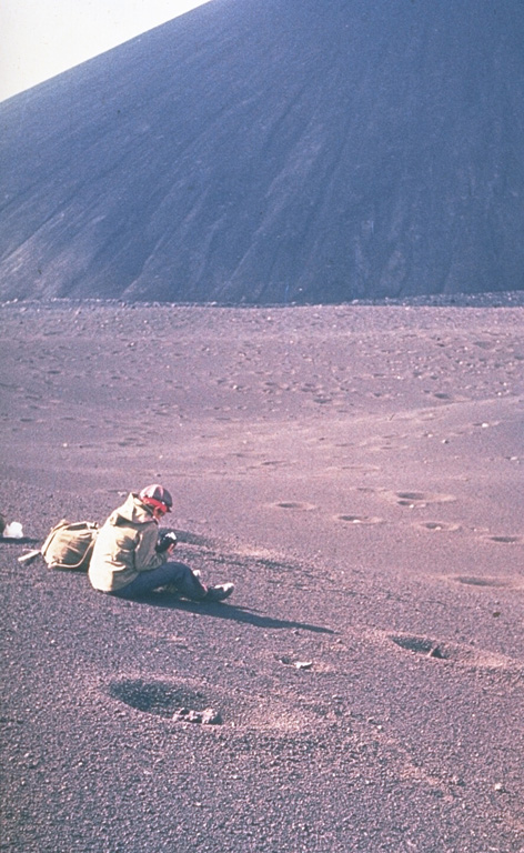A scientist from the Institute of Volcanology studies tephra produced during the 1975-76 eruption of Kamchatka's Tolbachik volcano. The circular pits were formed by the impact of dense volcanic blocks and bombs. The blocks, one of which can be seen in the closest pit, originated from the scoria cone in the background. Photo by Oleg Volynets, 1975 (Institute of Volcanology, Petropavlovsk).