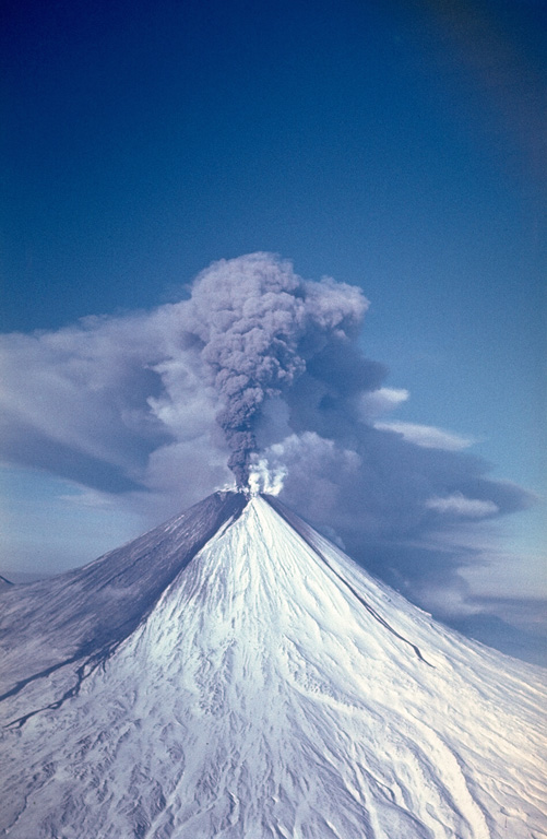 An ash plume erupting from the summit crater of Kamchatka's Kliuchevskoy volcano on 9 February 1987, traveling to the west. Ashfall from earlier eruptions darkens the southern flank of the volcano and several lahar deposits are visible. Explosive eruptions from the summit crater during 1986-1990 were accompanied by lava flows from both summit and flank vents. Photo by Alexander Belousov, 1987 (Institute of Volcanology, Kamchatka, Russia).