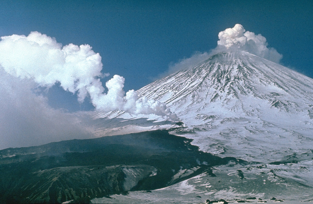 Gas-and-steam plume emissions occurred simultaneously from vents on the SW flank and the summit of Klyuchevskoy volcano in 1983. The SW-flank vent within a 200-m-long fissure produced the dark lava flow that melted the glacier surface, providing a channel for the lava flow and producing lahars that traveled 15 km. The flank eruption began on 8 March and was initially was restricted to a glacier gorge, but then bifurcated, forming a small lava field. Intermittent summit crater explosive activity had been occurring since October 1982. Photo by Yuri Doubik, 1983 (Institute of Volcanology, Petropavlovsk).